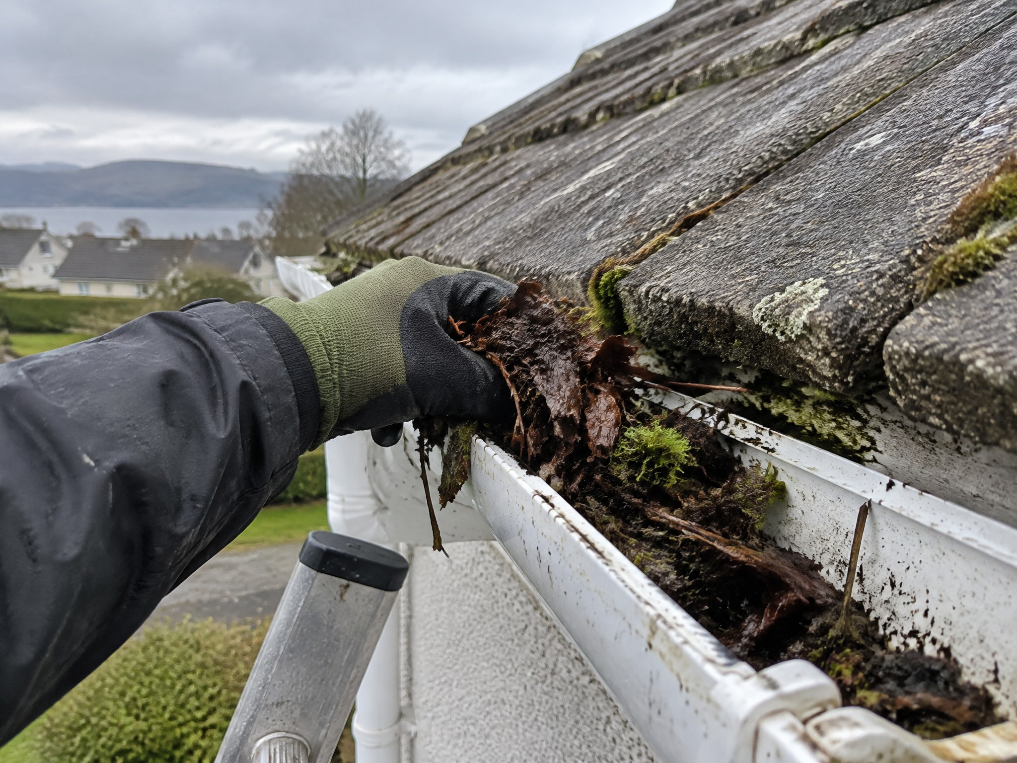 Gloved hand clearing leaves and moss from a white uPVC gutter
